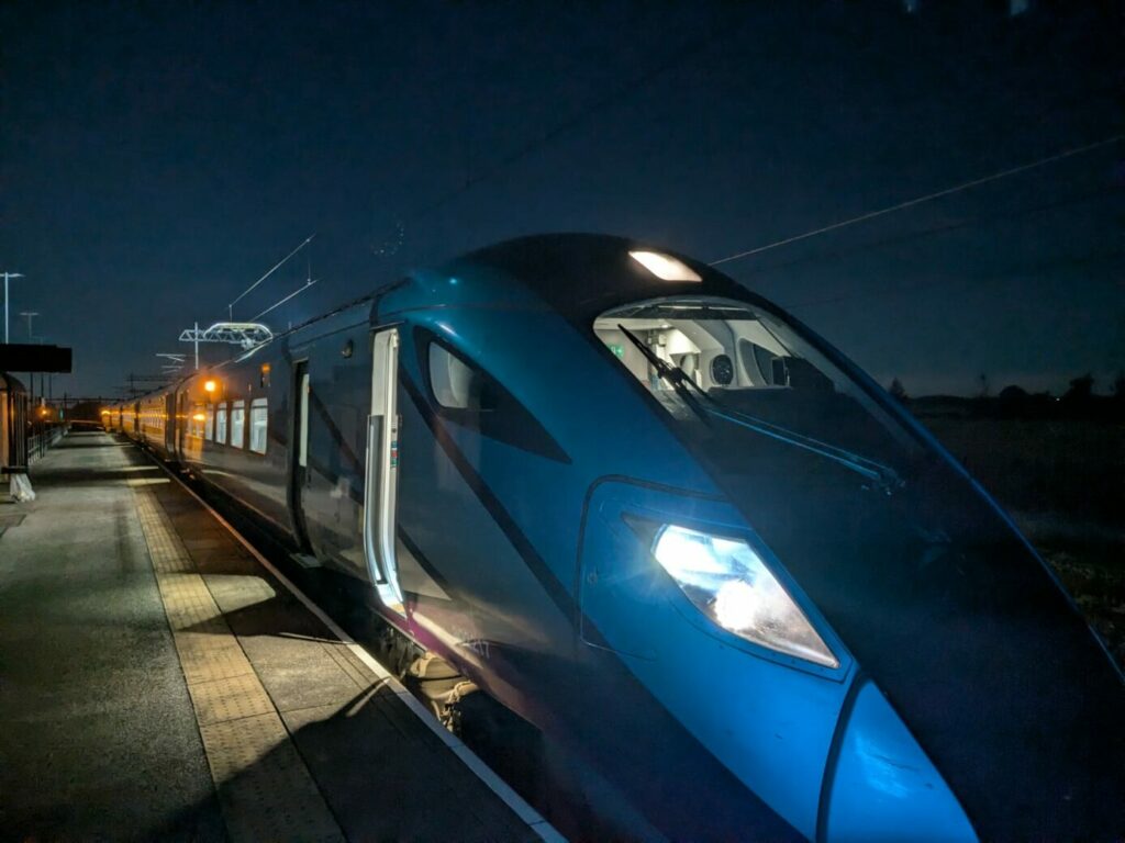 A blue train at a platform at night. The photo is taken from the nose of the train looking down the platform at a sharp angle.