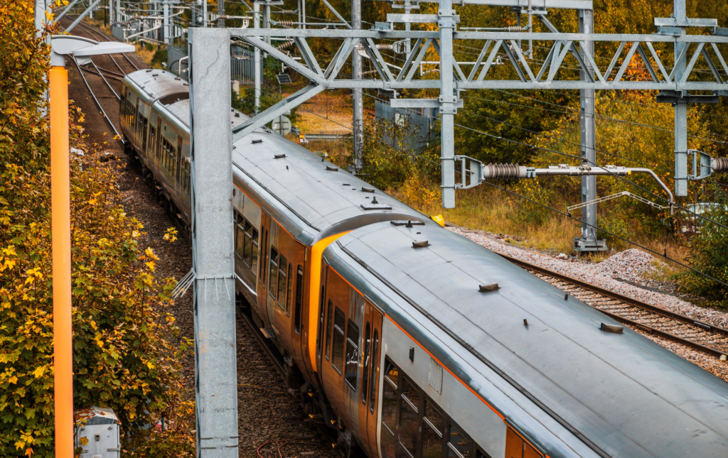 UK electric train from above overhead wires. It is autumn and the foliage around the tracks is orange and brown.