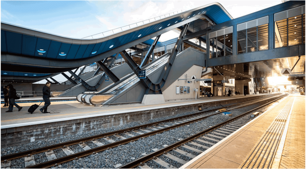 The photo depicts a train station platform outside, with escalators to go back inside the station.