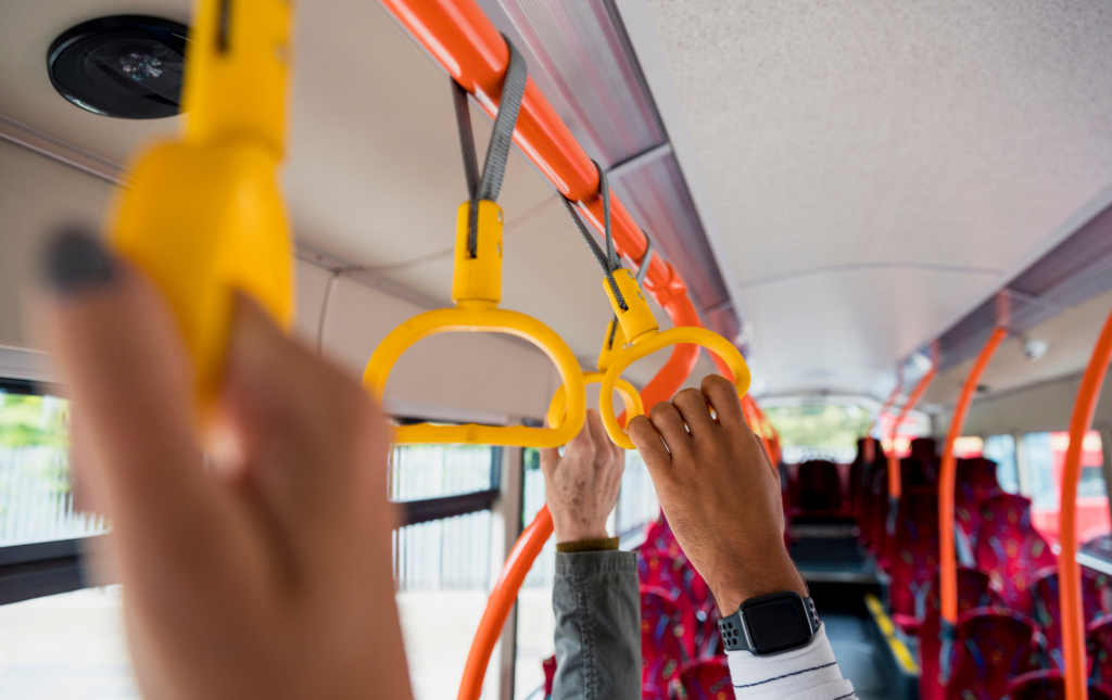 A photo of hands holding on to the handles above their heads on a bus