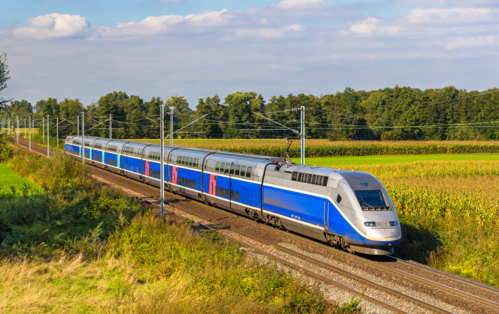 An image of a high speed train on a track going through luscious green fields in France. The train is mainly blue and silver.