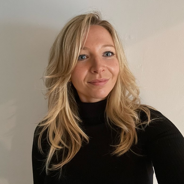 A selfie headshot photo of Annabel Snowden. She is weaiing a high neck, long sleeved black top, and is smiling at the camera.