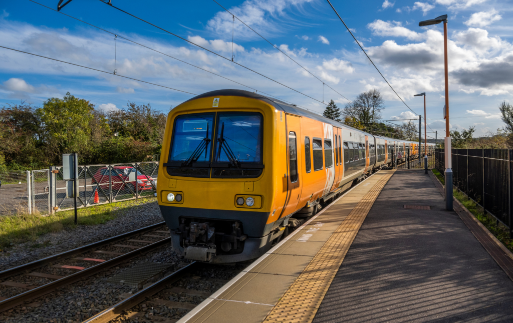 UK electric train at station platform. The train is yellow, it is a sunny day and the sky is blue.