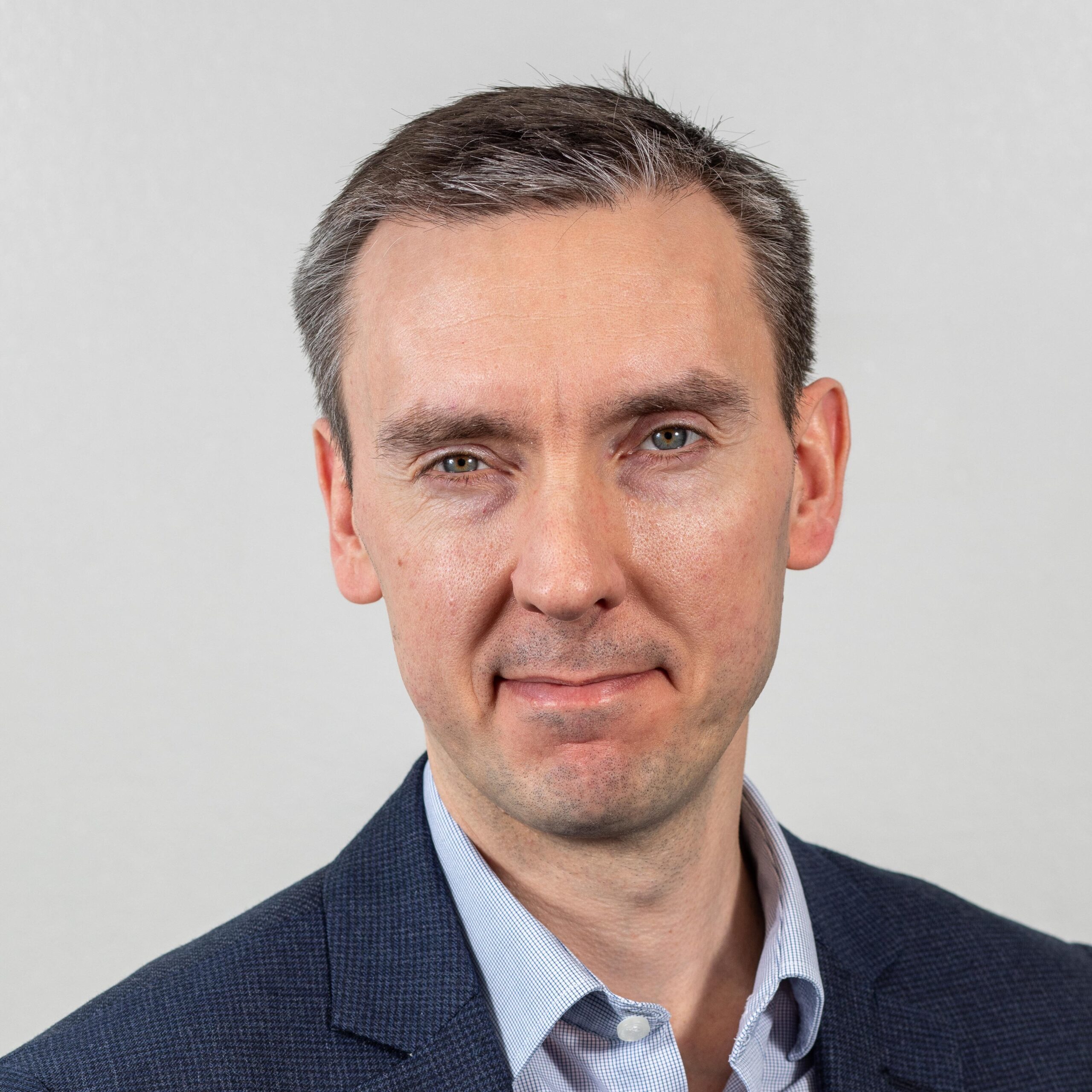 Headshot photo of Rob Dale. He is wearing a shirt and suit jacket and is smiling at the camera. The background is plain.